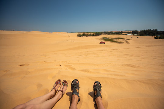 Close Up Portrait Of Legs,  Legs Of Couples Lying With A Mixture Of Golden Sand Dunes.Feet Of A Man And A Woman In Sandals On The Sand, Vietnam. Desert.