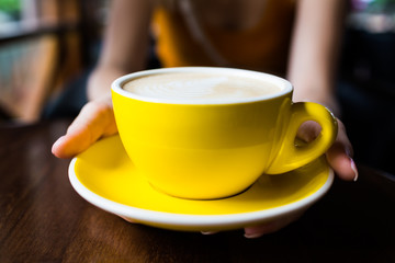 Yellow cup of aromatic coffee on a wooden table.