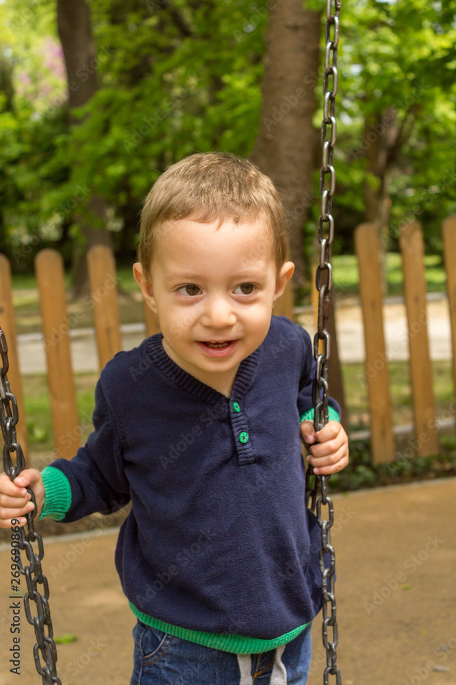 Wall mural little cute boy having fun on chain swings at the playground in a sunny spring day.