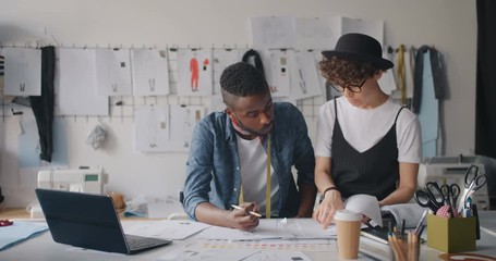 Male and female designers Caucasian and African American are communicating checking sketches using laptop working in modern workshop. People and job concept.