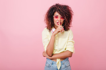 Adorable girl in pink cotton shirt telling secret. Sensual slim woman in casual summer outfit touching red lips with finger and looking with interest.