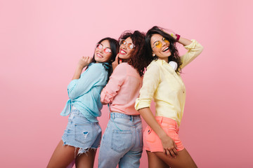 Carefree girls in colorful cotton shirts posing together and smiling. Indoor portrait of attractive young ladies expressing happy emotions during joint photoshoot.