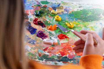 A young girl holds in his hand a palette-knife for drawing and mixes oiled paints. The process of mixing colors on the palette.