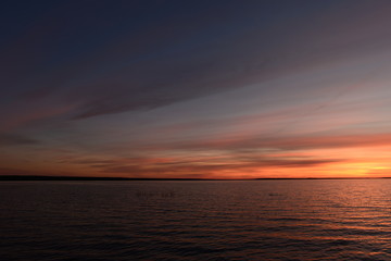 Cloudy sky in the twilight glow of the sun on the horizon above the water of the lake