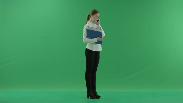 A young girl is talking on her phone handing her folders on the green screen