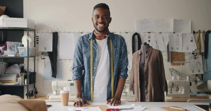 Portrait of male clothes designer looking at camera smiling standing in studio with tailor's dummy. Fashion design, profession and small business concept.