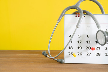 stethoscope and calendar on the table with yellow background, schedule to check up healthy concept