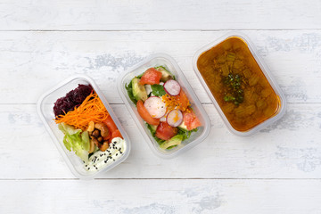 top view of three fast food dishes in plastic boxes. three portions are on a wooden white table. fast food and food delivery