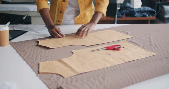 Male tailor manufacturing handmade clothing outlining model on material working in workshop alone using professional tools. People and profession concept.