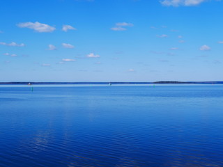 white clouds in the blue sky reflected on the surface of calm water