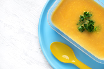 a piece of soup in a plastic box on a plastic plate and with a plastic spoon. free space for copy-paste. colored plastic tableware on white wooden table