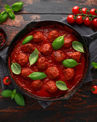 Homemade Meatballs in iron cast with sweet and hot tomato sauce, basil. On wooden table