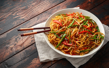Chow mein, noodles and vegetables dish with wooden chopsticks
