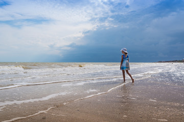 Beautiful seascape. Girl in dress and white hat on the beach over blue sky background