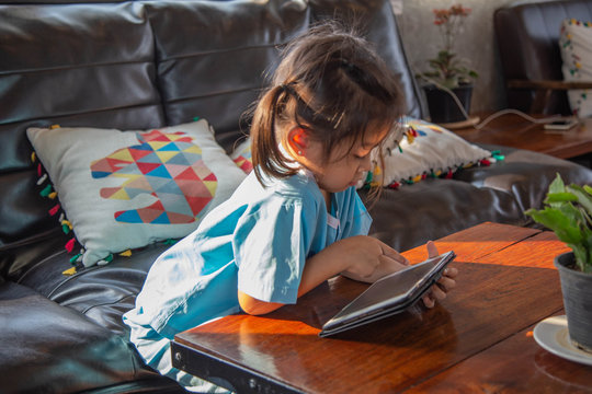 Little cute girl is smiling while playing game with digital tablet at home or watching an e-book and a smartphone at home on the sofa modern learning lifestyle concept
