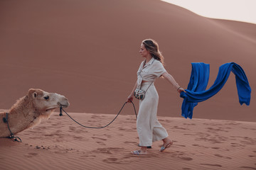 Caucasian young woman in linen clothes with camel in desert