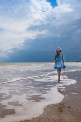 Beautiful seascape. Girl in dress and white hat on the beach over blue sky background