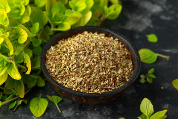 Fresh and dried oregano in bowl. on black rustic table