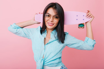 Close-up portrait of confident hispanic girl holding skateboard and laughing on bright pink...