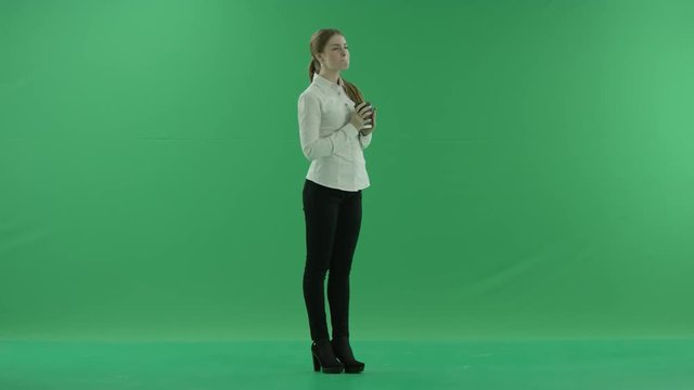 business woman is drinking a cup of coffee or tea. She wears formal dress: white shirt and blak trousers. Businesswoman think, got idea and smile over green screen