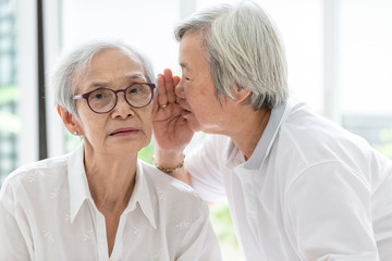 Asian senior woman holding hand  telling funny,gossips on ears to friend,speaking in elderly ear...