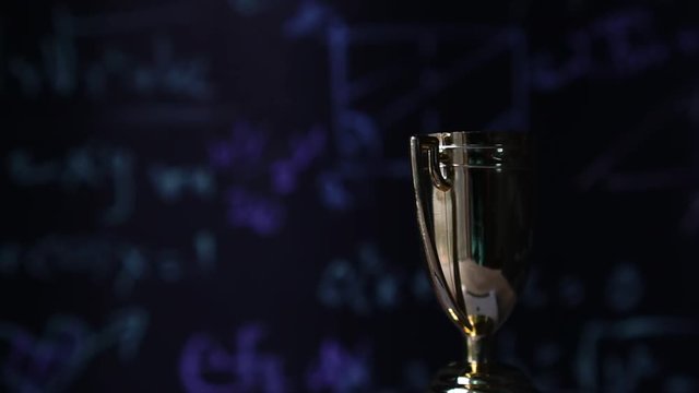 Achievement success in education awards concept: Rotating Golden trophy cup winner on blur formula equation blackboard background. Congratulation in university.