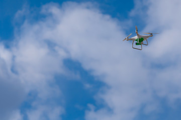 White drone with a green camera flying against the sky.