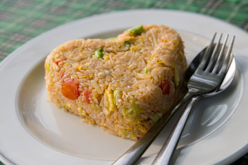 Fried rice cooked in heart shape. The plate is on a table.