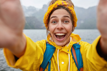 Young overemotive woman in yellow anorak and headband, stretches hands with unrecognizable device,...