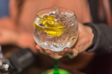 View of hand picking up a glass of refreshing gin, with lemon and lots of ice, classic glass