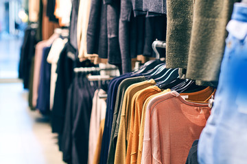 Interior of fashion clothes store with different women clothes on hangers in various colors.