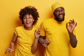 Photo of happy African couple dance together against yellow background, move body actively, show...