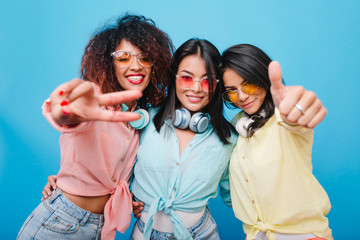 Lovable hispanic girl in cotton shirt posing between international female friends. Attractive african woman in pink attire having fun with other ladies.
