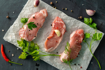 three fillet slices on a baking paper with spices and herbs on a black tables