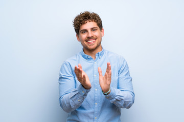 Blonde man over blue wall applauding after presentation in a conference