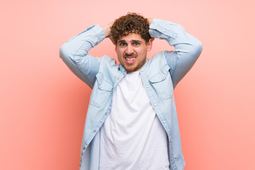 Blonde man over pink wall takes hands on head because has migraine