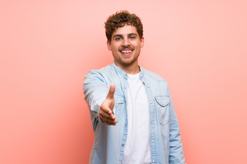 Blonde man over pink wall shaking hands for closing a good deal