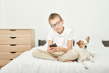 boy with a dog jack russell playing on a smartphone on a white bed at home