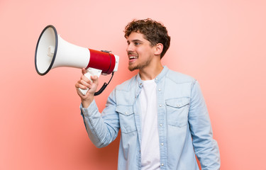 Blonde man over pink wall shouting through a megaphone