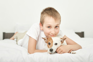 boy with dog jack russell sitting on a white bed at home