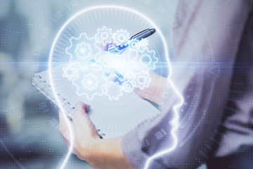Multi exposure of woman's writing hand on background with brain hologram. Concept of brainstorming.