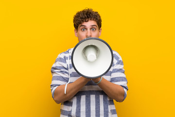 Blonde man over yellow wall shouting through a megaphone