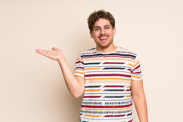 Blonde man over isolated wall holding copyspace imaginary on the palm to insert an ad