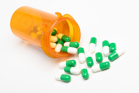 A bunch of green and white capsules spilling out of a slightly transparent orange medicine pharmacy bottle set on a plain white background in horizontal image format.