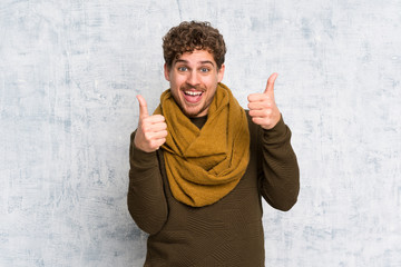 Blonde man over grunge wall with thumbs up gesture and smiling