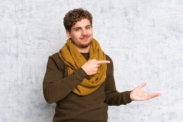 Blonde man over grunge wall holding copyspace imaginary on the palm to insert an ad