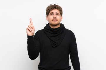 Blonde man over isolated white wall with fingers crossing and wishing the best