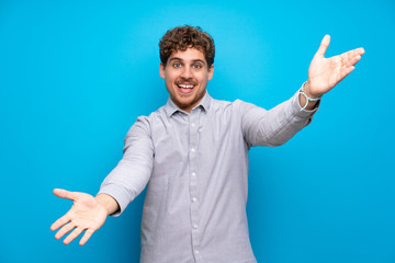 Fototapeta premium Blonde man over blue wall presenting and inviting to come with hand
