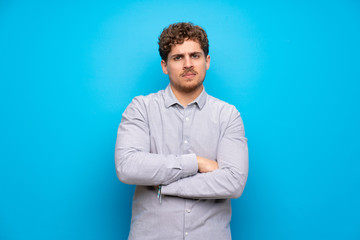 Blonde man over blue wall feeling upset