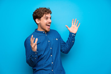 Blonde man over isolated blue wall with surprise facial expression
